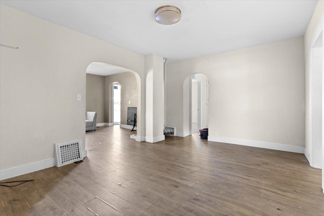 unfurnished room with arched walkways, visible vents, baseboards, and wood finished floors