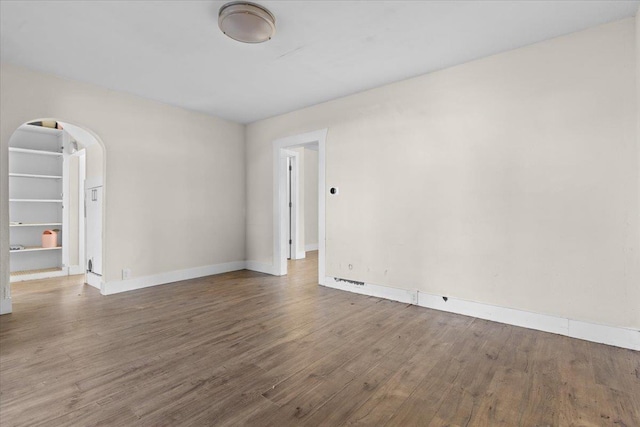 spare room with arched walkways, wood finished floors, and baseboards