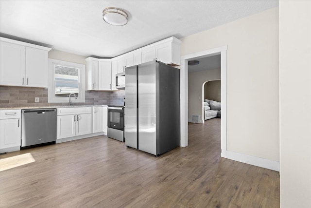 kitchen with light wood finished floors, white cabinetry, stainless steel appliances, and backsplash