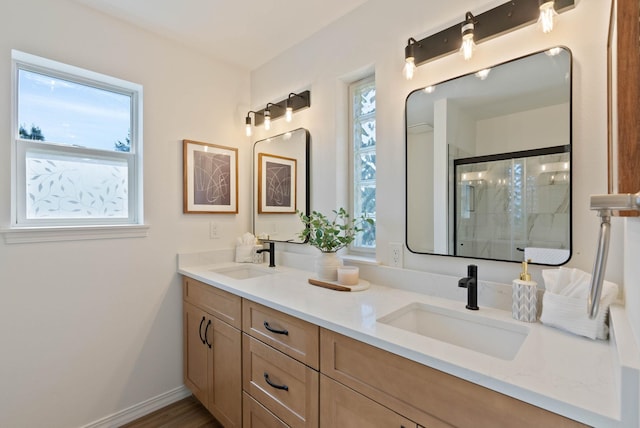 full bath with double vanity, a shower stall, baseboards, and a sink