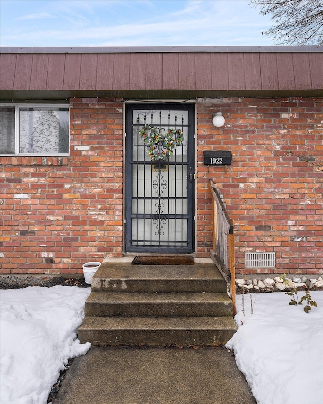 doorway to property featuring brick siding and visible vents