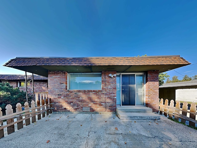 view of front of house featuring a shingled roof, a patio, and brick siding