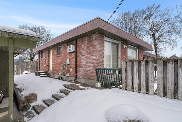 view of snow covered exterior featuring an AC wall unit, brick siding, and fence