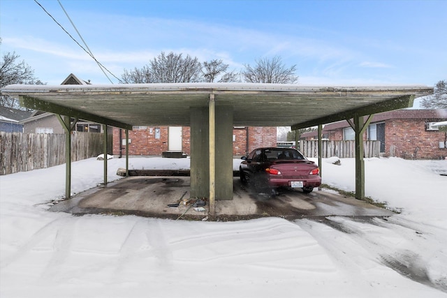 snow covered parking area featuring fence and a carport