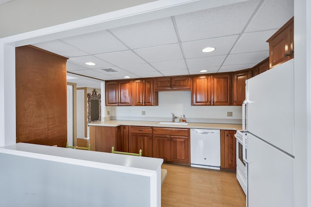 kitchen featuring white appliances, brown cabinets, light countertops, light wood-style floors, and a sink