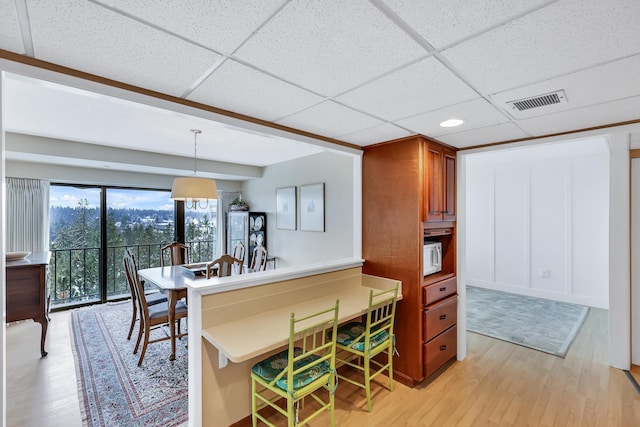 kitchen with visible vents, a drop ceiling, light wood-style flooring, a breakfast bar area, and brown cabinets