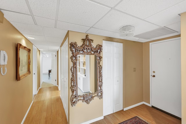 hallway with a drop ceiling, light wood-type flooring, and baseboards