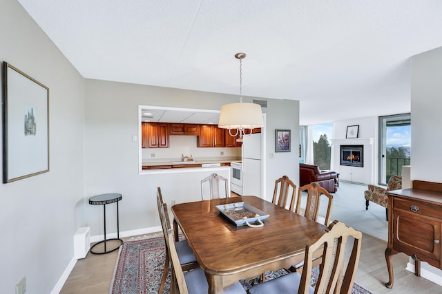 dining area featuring a warm lit fireplace, baseboards, visible vents, and light wood-style flooring