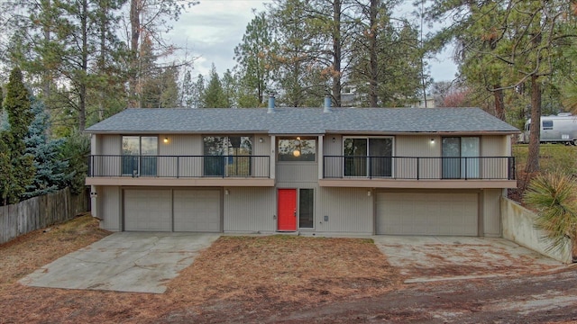 view of front of property featuring a garage, a balcony, fence, and concrete driveway