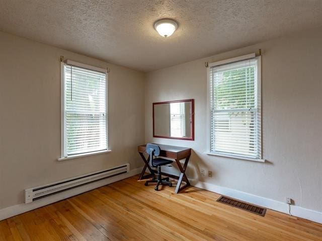 office space with visible vents, baseboard heating, a textured ceiling, wood finished floors, and baseboards