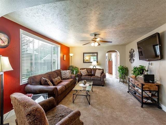 living area featuring carpet, a textured ceiling, arched walkways, and a ceiling fan