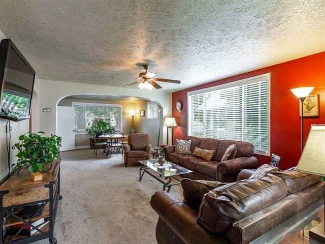 carpeted living area featuring a ceiling fan, arched walkways, and a textured ceiling