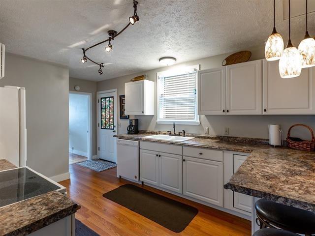 kitchen featuring dark countertops, light wood-style floors, white cabinetry, a sink, and white appliances