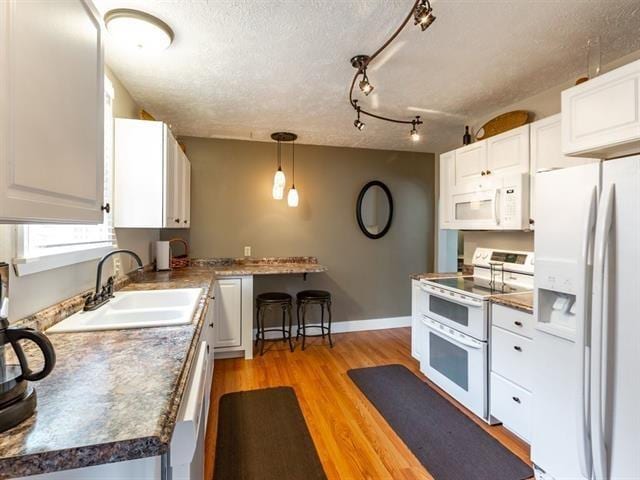 kitchen with white appliances, a sink, baseboards, white cabinets, and light wood-type flooring