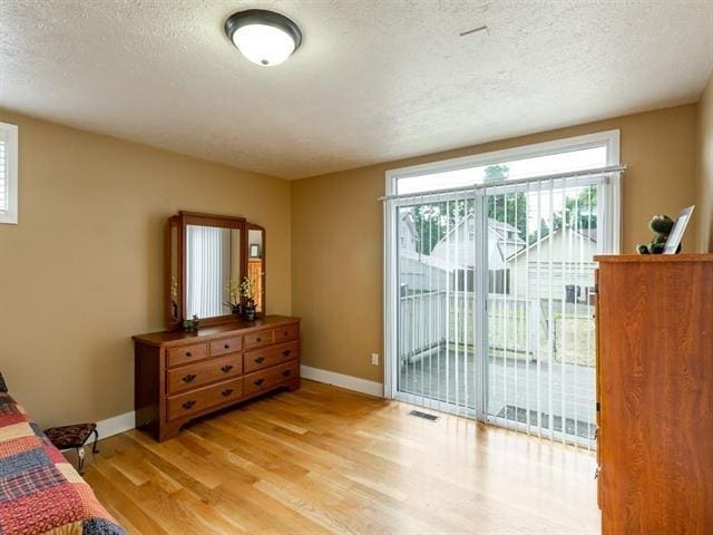 bedroom with light wood finished floors, baseboards, visible vents, access to exterior, and a textured ceiling