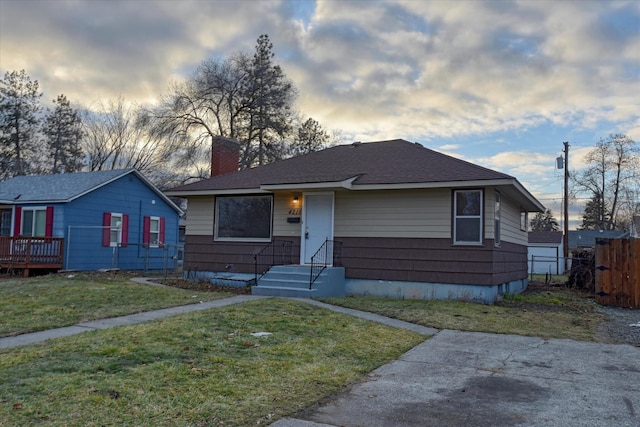 view of front of house featuring a shingled roof, a chimney, fence, and a front lawn