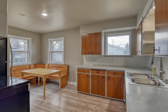 kitchen featuring light countertops, black range with electric stovetop, light wood-style flooring, freestanding refrigerator, and a sink