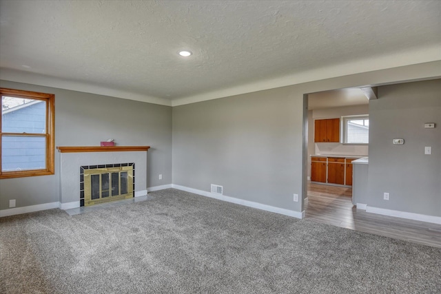 unfurnished living room with carpet floors, a tiled fireplace, visible vents, and baseboards