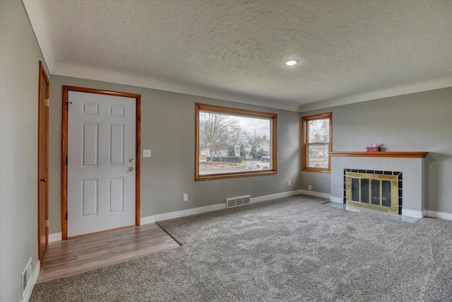 unfurnished living room with baseboards, a textured ceiling, visible vents, and a tiled fireplace