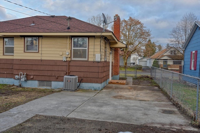 view of side of home featuring central AC unit, a shingled roof, fence, a chimney, and a patio area