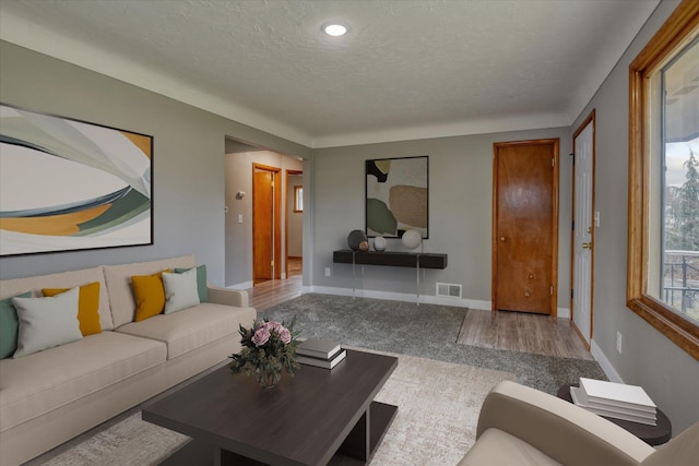 living room with a textured ceiling, visible vents, and baseboards