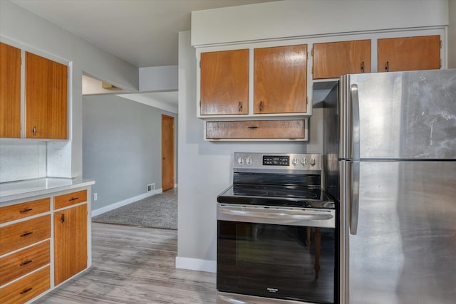 kitchen featuring stainless steel appliances, light countertops, light wood-style flooring, brown cabinetry, and baseboards