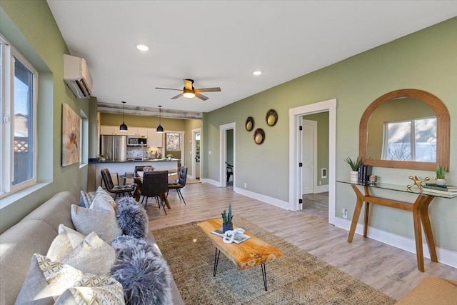 living area featuring a wall unit AC, a healthy amount of sunlight, light wood-style flooring, and baseboards