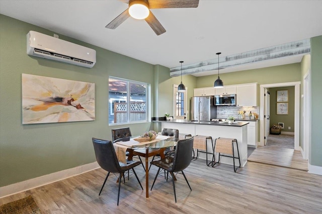dining area featuring a ceiling fan, baseboards, light wood finished floors, and a wall mounted AC