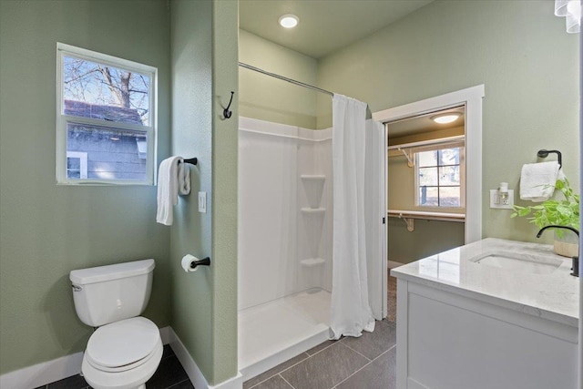 bathroom featuring toilet, a stall shower, vanity, baseboards, and tile patterned floors
