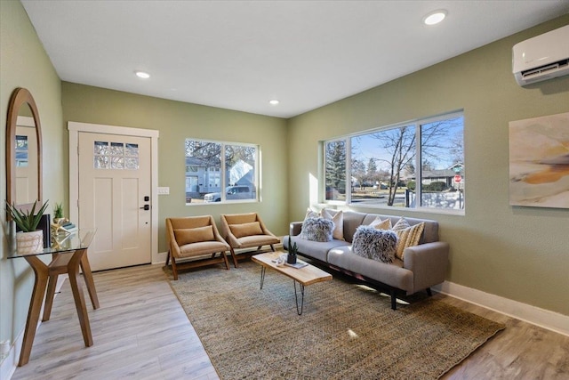 living area with light wood-type flooring, an AC wall unit, baseboards, and recessed lighting