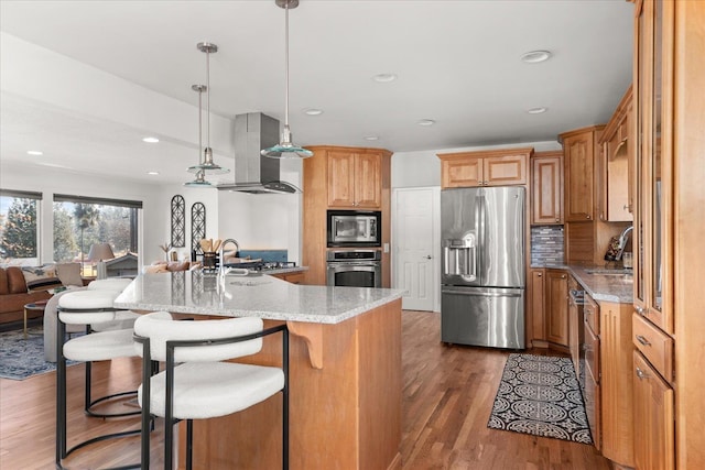 kitchen featuring appliances with stainless steel finishes, a sink, wall chimney range hood, and wood finished floors