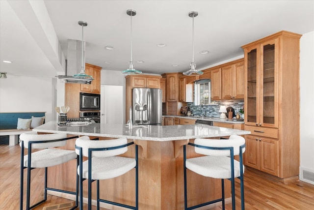 kitchen with light wood-style flooring, light stone counters, glass insert cabinets, stainless steel appliances, and backsplash