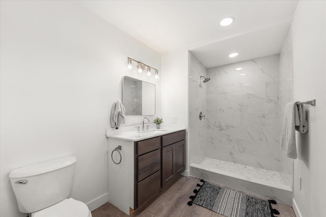 full bath featuring toilet, wood finished floors, vanity, baseboards, and a tile shower