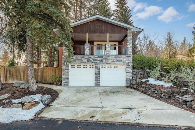 view of front of house featuring an attached garage, a balcony, fence, stone siding, and concrete driveway