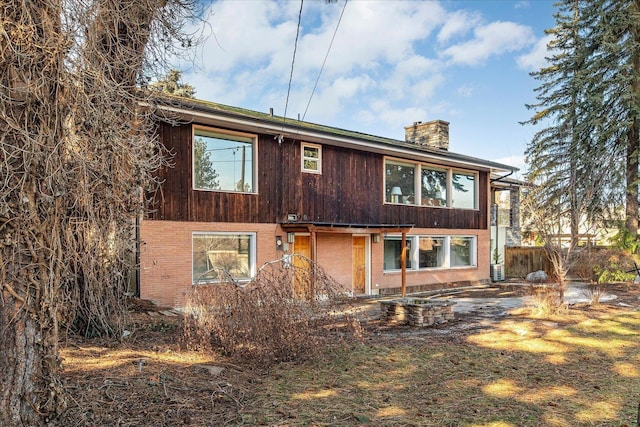 view of front of house featuring brick siding, a chimney, and fence