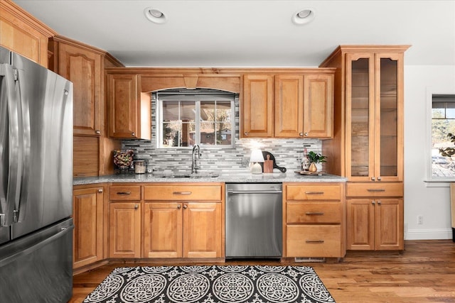 kitchen with stainless steel appliances, wood finished floors, a sink, and light stone countertops