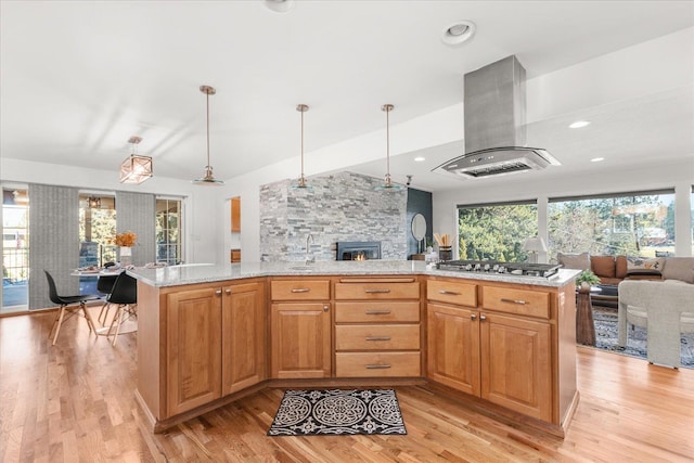 kitchen featuring stainless steel gas cooktop, hanging light fixtures, light wood-style floors, open floor plan, and exhaust hood