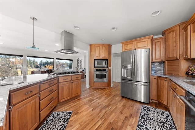 kitchen with light wood-style flooring, stainless steel appliances, a sink, wall chimney range hood, and light stone countertops