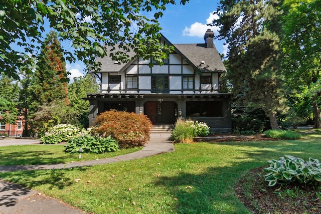 tudor house featuring a shingled roof, a front yard, and a chimney