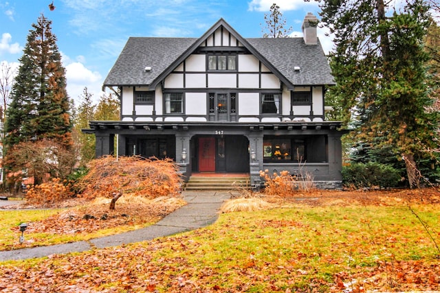 tudor home with roof with shingles, a chimney, and a front lawn