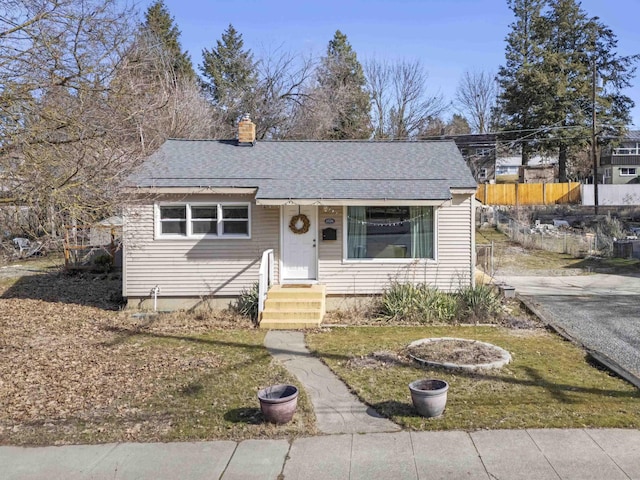 view of front of property with roof with shingles, a chimney, and fence