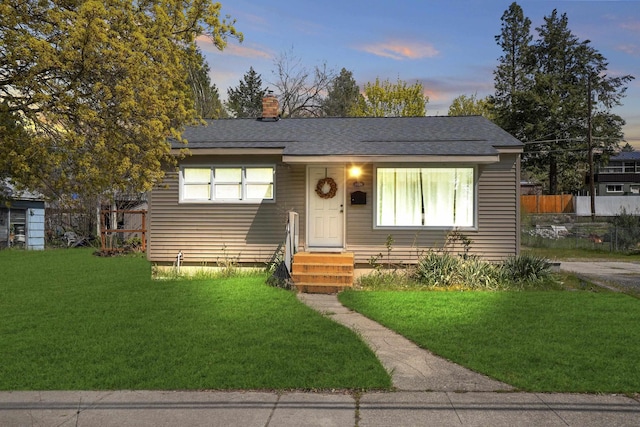 bungalow-style house with a chimney, a front lawn, fence, and a shingled roof