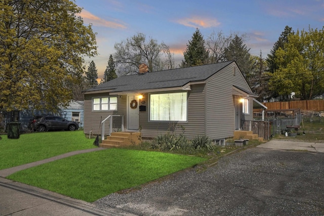 bungalow-style house with a yard, roof with shingles, a chimney, and fence