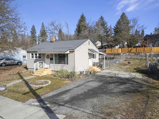 bungalow-style home with a chimney, fence, and a shingled roof