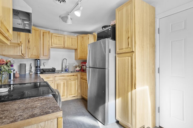 kitchen featuring dark countertops, visible vents, light brown cabinetry, freestanding refrigerator, and a sink