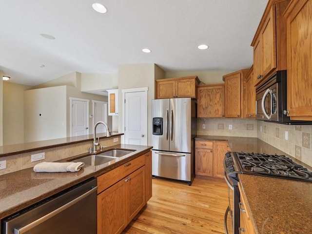 kitchen with light wood finished floors, tasteful backsplash, brown cabinets, stainless steel appliances, and a sink