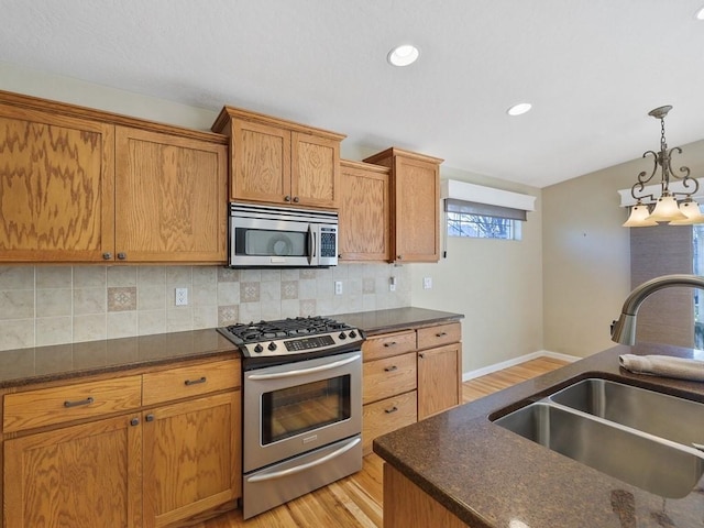 kitchen with light wood-style flooring, a sink, hanging light fixtures, appliances with stainless steel finishes, and tasteful backsplash