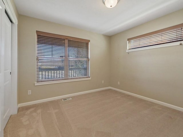 unfurnished room with carpet, visible vents, and baseboards