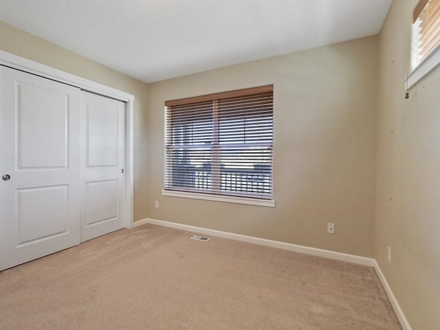 unfurnished bedroom with light carpet, a closet, visible vents, and baseboards