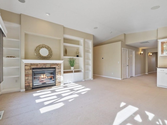 unfurnished living room featuring built in features, lofted ceiling, light colored carpet, a stone fireplace, and baseboards